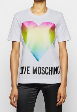 Personne portant un t-shirt blanc avec un grand imprimé cœur multicolore et le texte "LOVE MOSCHINO" en noir en bas.