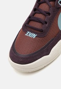 Nike tenisice s gornjim dijelom od smešnog mrežastog materijala, tamnoljubičastim akcentima od suede-a, tirkiznim logotipom i teksturiranim belim međuslojem s flekama.