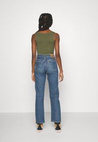 Olijfgroen tanktop, gecombineerd met hooggesneden blauwe denim jeans met een leren patch. Draag het met zwart-witte canvas schoenen.