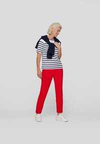Striped navy and white t-shirt paired with red trousers. A navy sweater draped over the shoulders. White sneakers complete the look.