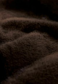 Brown faux fur material with a soft, dense texture, featuring subtle variations in shade and natural, fluffy strands.