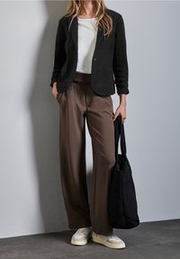 Svart blazer, vit skjorta, bruna vida byxor, vita sneakers och en kviltad svart tote-väska. Släta texturer och välsittande design.