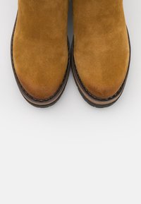 Brown suede ankle boots with a rounded toe, featuring a stitched trim and a layered light and dark brown rubber sole.