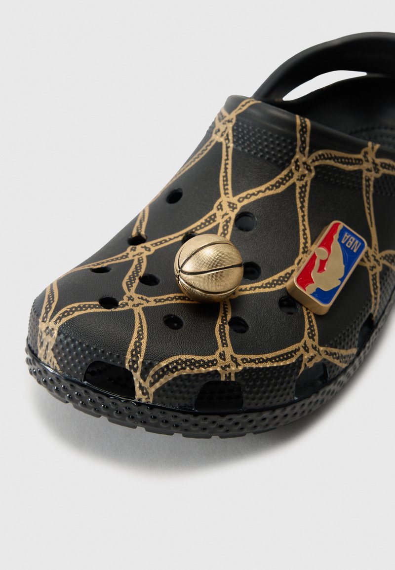 Schwarze Crocs mit einem goldenen Basketballnetz-Muster, ausgestattet mit einem goldenen Basketball-Anhänger und einem NBA-Logo-Patch auf der Oberseite.