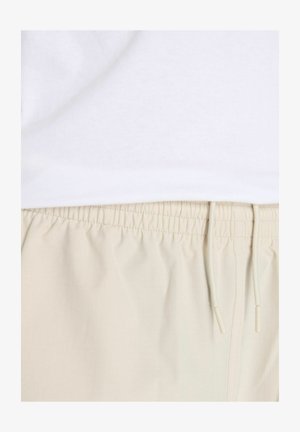 Beige shorts med elastisk talje og en glat tekstur samt justerbar snor, båret under en almindelig hvid t-shirt.