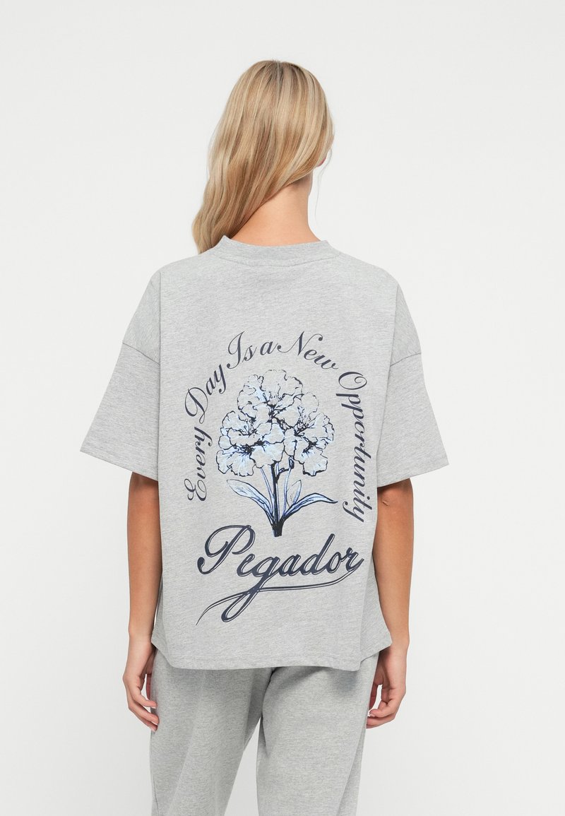 Grå oversized t-skjorte laget av bomull, med blomstermønster og skriftlig tekst på baksiden, med avslappet passform og korte ermer.