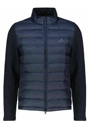 Navy padded vest with zip closure, featuring a textured dark gray knit fabric on sleeves and collar, and a small logo on the chest.