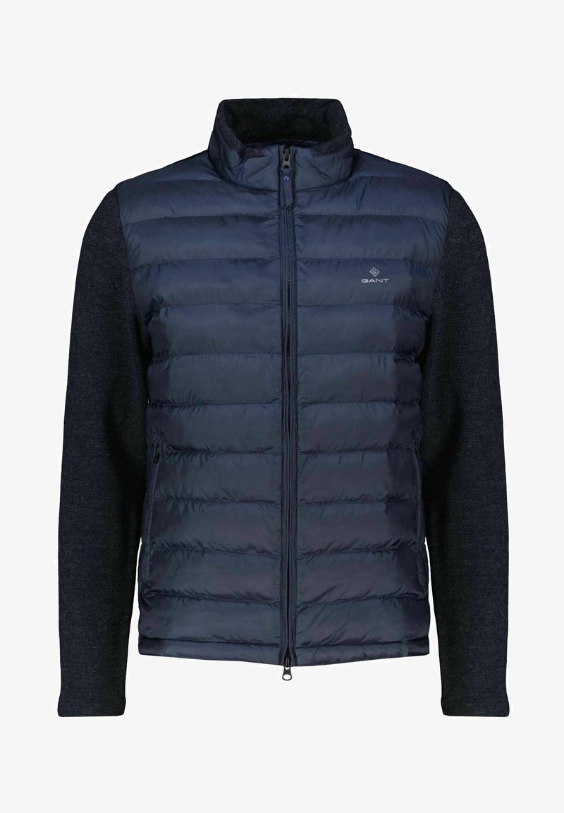 Navy padded vest with zip closure, featuring a textured dark gray knit fabric on sleeves and collar, and a small logo on the chest.