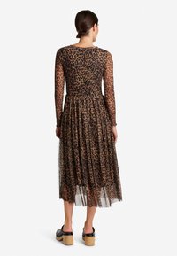 Pitkähihainen mekko puolijäykästä ruskeasta kankaasta, jossa on musta leopardikuosi, vyötäröllä kiristetty ja valuva helma. Yhdistetty mustiin korokepolkimiin.