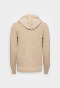 Beige ribbad huvtröja med en texturerad yta och en dragkedja i huvan. Har långa ärmar och en nederkant med kontrasterande ribb.