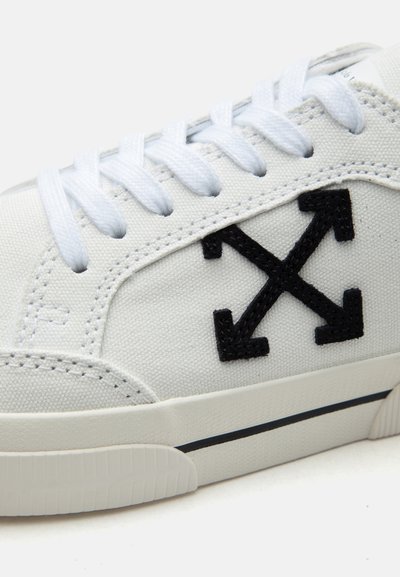 Άσπρο αθλητικό παπούτσι με άσπρα κορδόνια, μαύρο λογότυπο με σταυρωτό βέλος στο υφασμάτινο πλάι και υφασμένο λευκό πέλμα με λεπτή μαύρη ρίγα.