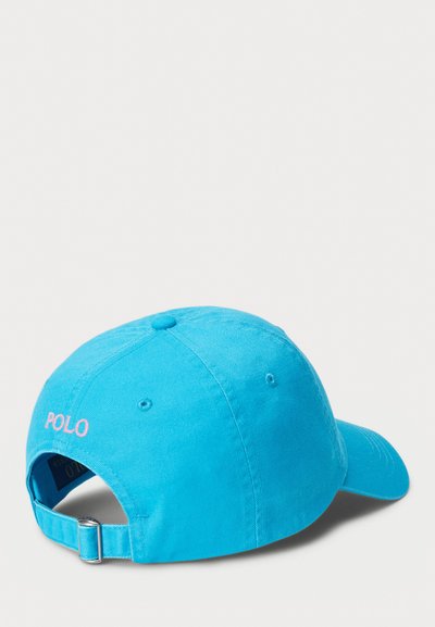 Šviesiai mėlyna beisbolo kepuraitė, pagaminta iš medvilnės. Šiuo atveju yra reguliuojama juosta gale ir išsiuvinėtas „POLO“ logotipas rožinės spalvos šone.