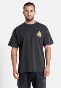 Zwarte katoenen t-shirt met korte mouwen, voorzien van een gouden grafisch ontwerp op de borst. Relaxte pasvorm, ronde halslijn en zachte textuur.