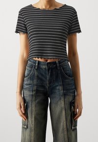 Černobílý crop top s proužky a žebrovanou texturou, s vroubkovaným okrajem, kombinovaný s volnými modrými cargo džínami s kapsami.