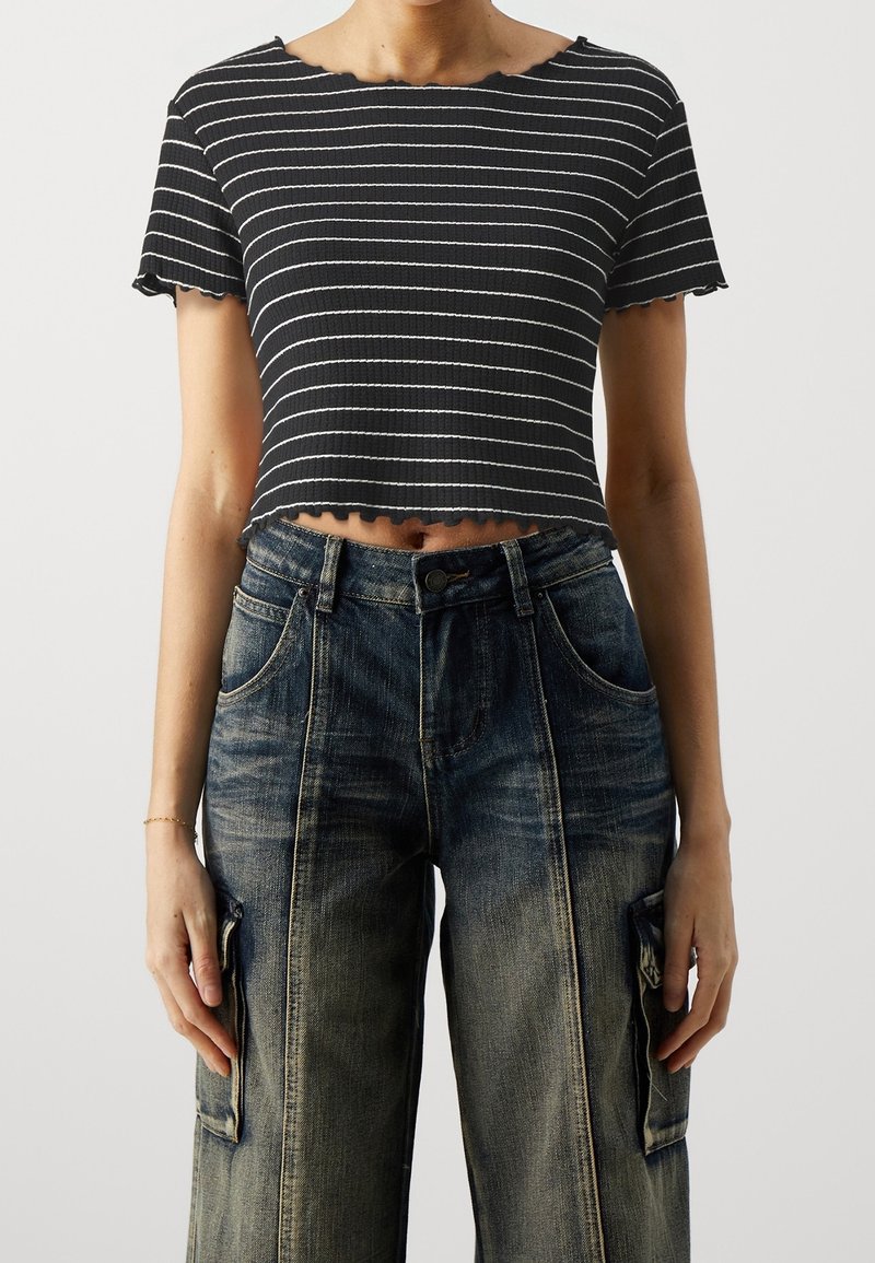 Černobílý crop top s proužky a žebrovanou texturou, s vroubkovaným okrajem, kombinovaný s volnými modrými cargo džínami s kapsami.