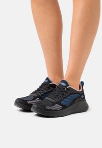 Black athletic shoes with mesh upper, blue stripes, textured sole, and pink accents. Laced design, suitable for active wear.