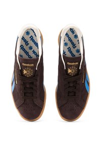 Sneaker in suede marrone con accenti blu, punta perforata, lacci marroni e suola in gomma color caramello con il branding dorato Reebok sulla linguetta.