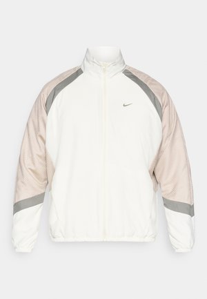 Witte jas met mesh beige mouwen, grijze accenten, staande kraag, volledige rits en elastische manchetten. Heeft een klein logo op de borst.