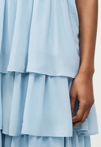 Donkere hand rust naast lichtblauwe gelaagde chiffonjurk met zachte, vloeiende stof.