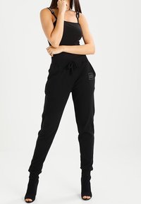 Black sportswear featuring a fitted tank top with logo straps and relaxed joggers with a drawstring waist and patch detail on the side.
