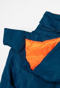 Blue jacket collar with Velcro strap and bright orange inner lining, showing zipper and stitching details on a white background.