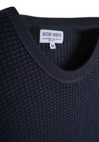 Maglione a maglia testurizzata blu scuro con collo a V e un'etichetta interna che mostra il marchio e la taglia M.