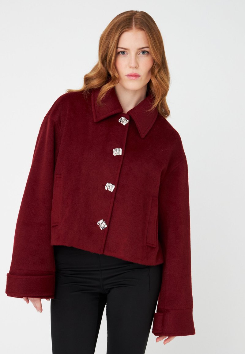 Burgundy cropped jacket made of soft fabric, featuring a wide collar and shiny silver buttons. Includes two front pockets and wide sleeves.