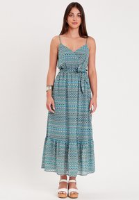 Robe maxi avec des fines bretelles, motif géométrique bleu et vert, taille froncée et ourlet en étagères, fabriquée en tissu léger. Sandales à plateforme blanches.