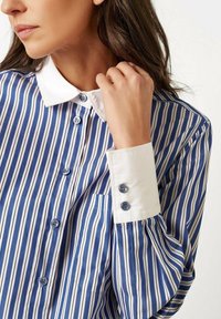 Blue and white striped shirt with a white collar, featuring button closures and cuff accents. Smooth fabric with a vertical pattern.