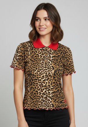 Woman with shoulder-length brown hair wearing a leopard print polo shirt with a red collar and red-edged sleeves, smiling slightly.