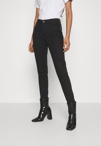 Pantalones negros ajustados con un diseño entallado, que cuentan con un cierre de botón, bolsillos laterales y una textura suave. Combinados con botas de tacón negras.