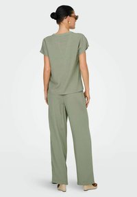 Ljusgrön, löst sittande topp och vida byxor. Mjuk textur, korta ärmar och bekväm passform. Bärs med sandaler med blockklack i tan.