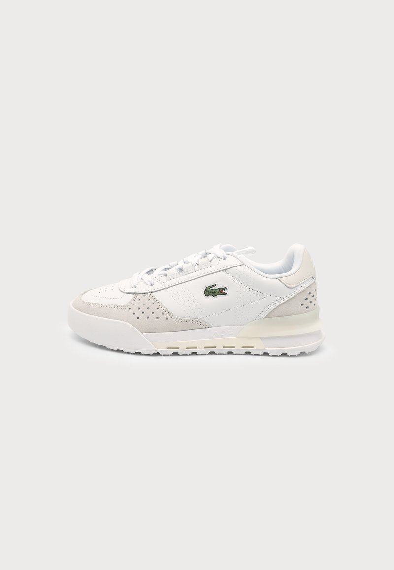 Baskets basses blanches et beiges avec lacets et logo crocodile vert sur le côté, présentées sur un fond clair.