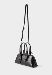 Svart lærhåndveske med to håndtak og en avtakbar skulderrem. Har en gullglidelås og aksentueringstropper med nagle detaljer.