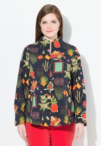 Camicia button-up colorata con motivi floreali e di frutta su uno sfondo scuro, con colletto alla coreana e maniche lunghe. Abbinata a pantaloni rossi.