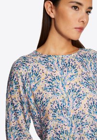 Langärmliges Oberteil mit Blumenmuster in Pastellrosa, mit blauen und gelben botanischen Designs. Weicher Stoff mit rundem Ausschnitt.