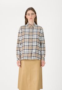 Beige and white plaid shirt with navy and red accents, button-up front, long sleeves, and a collar, paired with a tan leather skirt.