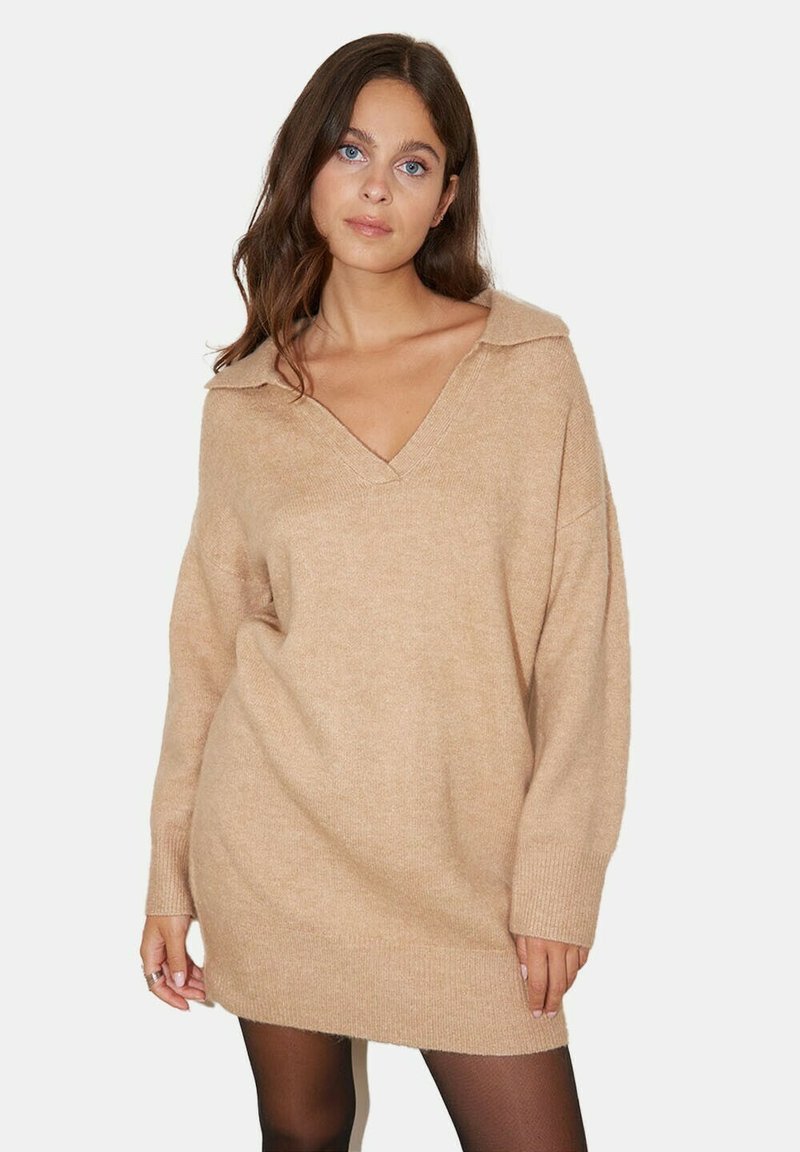 Robe-pull surdimensionnée beige avec un col en V et un col montant. Texture douce, poignets et ourlet côtelés. Manches longues. Finition lisse.