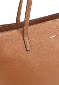 Bruine leren tote bag met twee handvatten, voorzien van een gestructureerd oppervlak en crèmekleurige stiksels, en een klein metallic logo-accent.