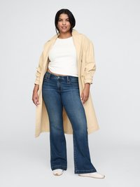 Beige trench coat fehér felső és sötétkék trapéznadrág felett, laza fazonnal és világos színű sportcipőkkel. Simább szövettextúra.