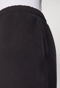 Pantalones de chándal negros con cintura elástica, hechos de una tela suave. Cuenta con bolsillos laterales y una textura suave y mate.