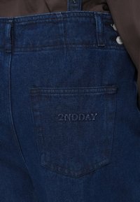 Tmavé džíny s rovný střih, s zadní kapsou s embosovaným nápisem "2NDAY." Textura vypadá hladce s mírným odbarvením.