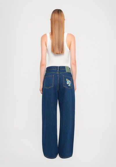 Laiad sinised denim püksid on kõrge vöökohaga, kaks tagakotti erksate tikanditega ning roheline brändi silt tagavöökoha peal.