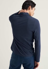 Sötétkék hosszú ujjú galléros póló sima anyagból, klasszikus gallérral és laza nyakkivágással, hozzá illő kék nadrággal párosítva.