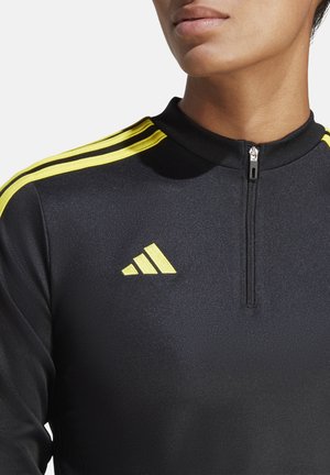 Giacca a track nera con zip, caratterizzata da strisce gialle e un grande logo Adidas sul petto. Realizzata in un tessuto liscio e strutturato.
