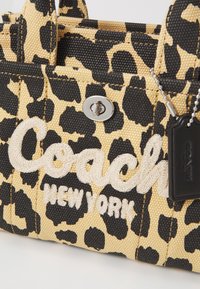 Leopárdmintás kézitáska fekete és világosbarna szőtt anyagból, fehér hímzett "Coach New York" szöveggel és ezüst színű fém részletekkel.