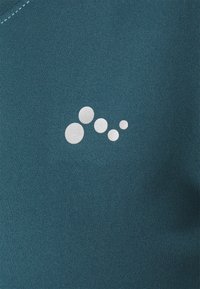 Türausgestatteter, glatter Stoff in Türkis. Ein weißes, kreisförmiges Grafikdesign mit unterschiedlichen Größen, das sich zur einen Seite hin positioniert.