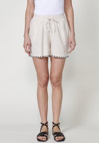 Short beige clair avec une taille élastique et un cordon de serrage, doté d'une finition texturée et d'un passepoil noir décoratif à l'ourlet.