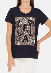 Granatowa bawełniana koszulka z krótkim rękawem, z prostokątnym wzorem z cekinów w kolorze różowego złota, z czarnymi literami ułożonymi wewnątrz cekinów.