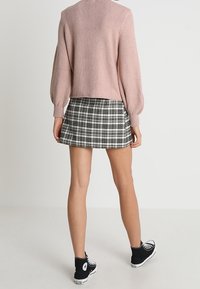 Jasnoróżowy sweter na drutach z balonowymi rękawami, w połączeniu z czarno-białą mini spódniczką w kratę i czarnymi tenisówkami z płótna.